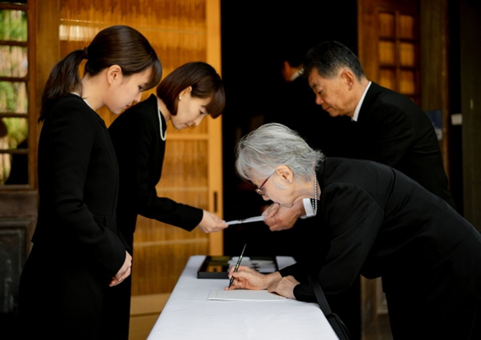 メモサのお葬式が松戸市の斎場で受付を案内する黒服のスタッフと記帳する遺族の様子。